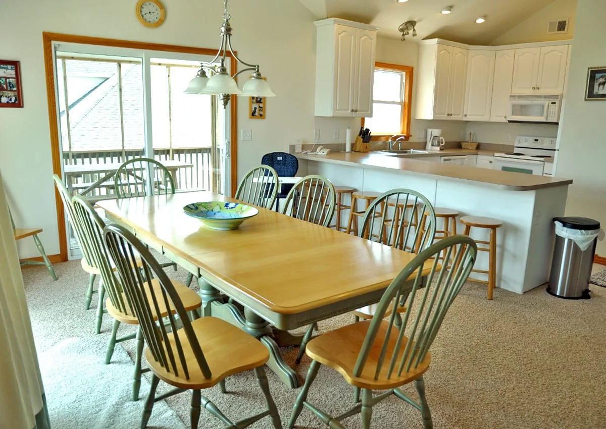 A dining area with a wooden table and chairs beside an open kitchen.