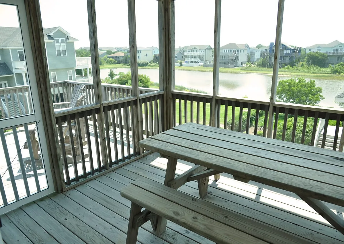 A wooden deck with a picnic table overlooks a lake and nearby houses.
