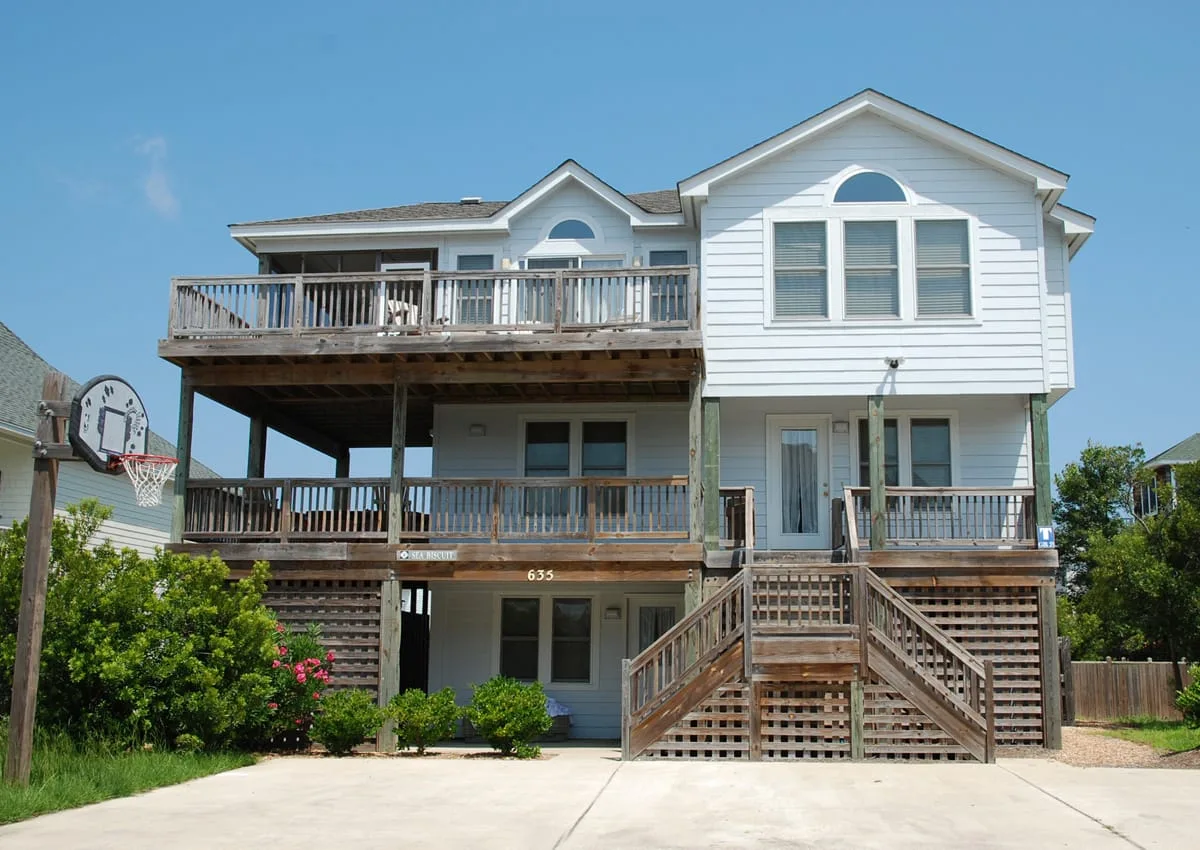 A large white house with raised wooden decks and exterior stairs.