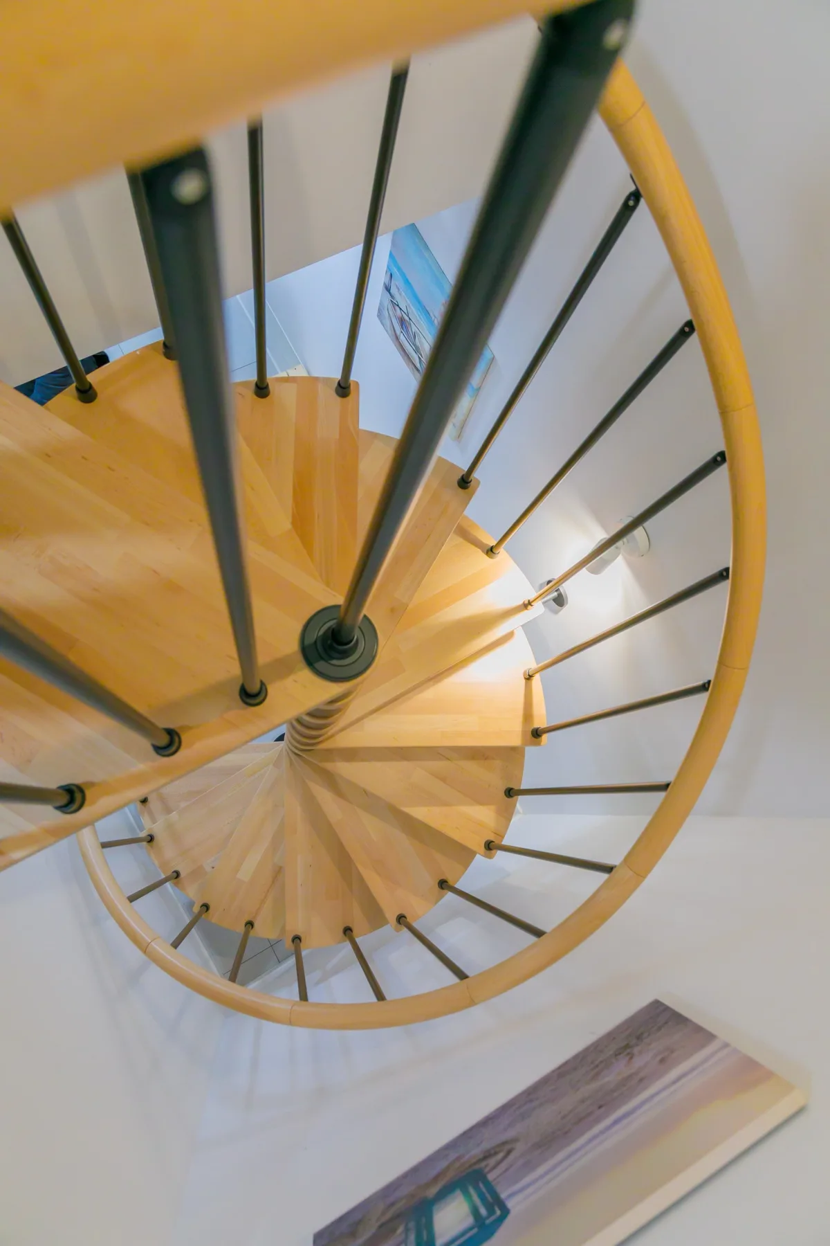 Una escalera curva de madera con barandillas metálicas oscuras, vista desde arriba.