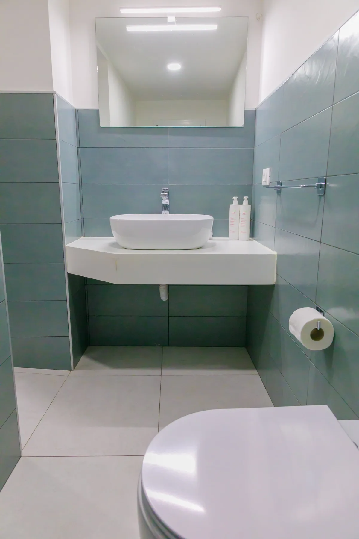 Un baño con azulejos, lavabo suspendido y espejo.