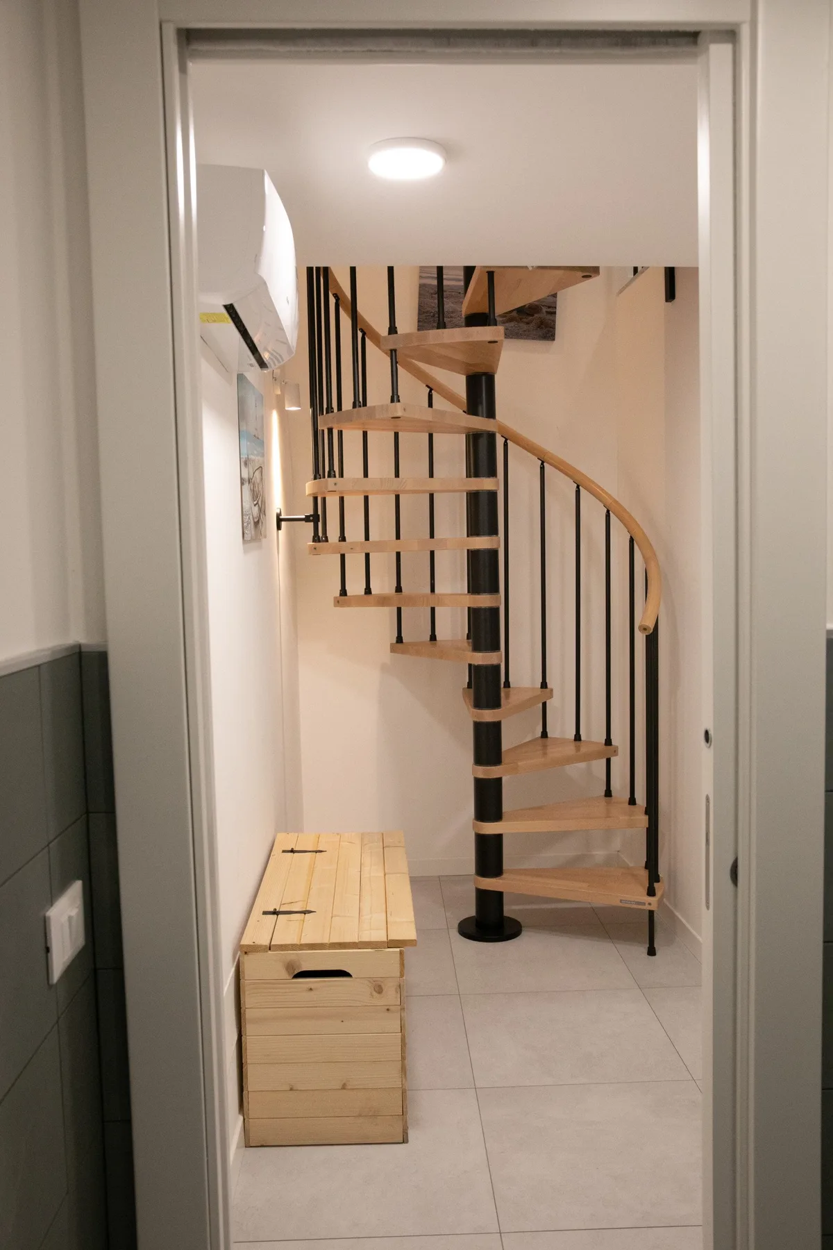 Un pasillo con suelo de baldosas da a una escalera de caracol con peldaños de madera.