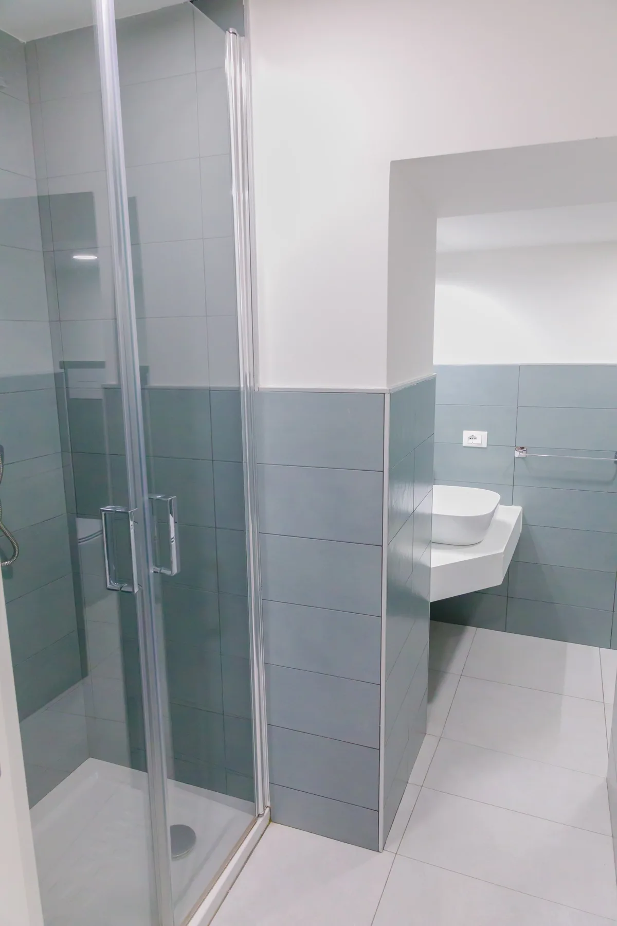 Un baño alicatado con ducha de vidrio y lavabo suspendido.