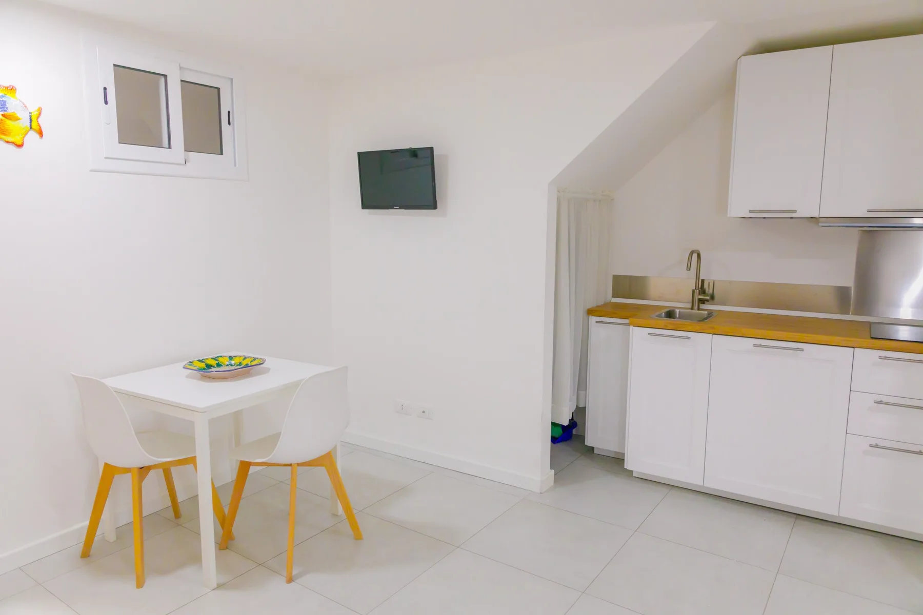Una cocina y comedor luminosos con gabinetes blancos y una mesa pequeña.