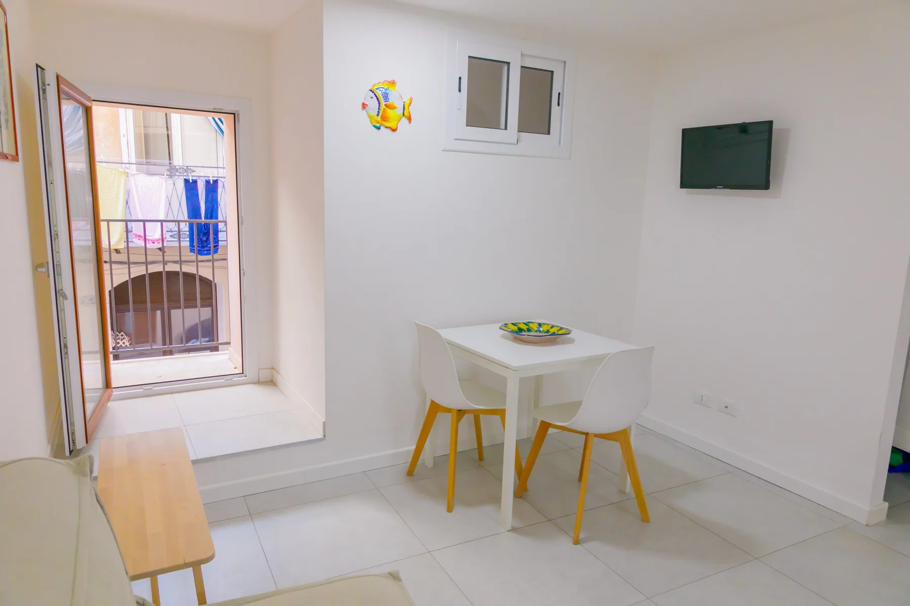 Un pequeño comedor con una mesa blanca y sillas junto a una ventana abierta.