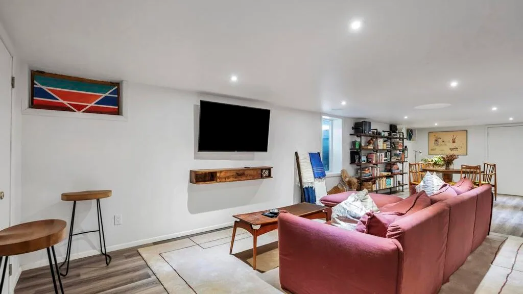 Una sala de estar con asientos rosados, una mesa de centro y un televisor en la pared.