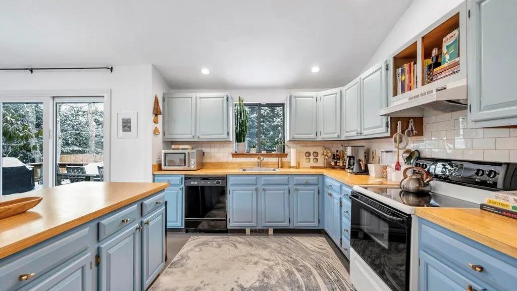 Una cocina luminosa con gabinetes claros, encimeras de madera y una ventana central.
