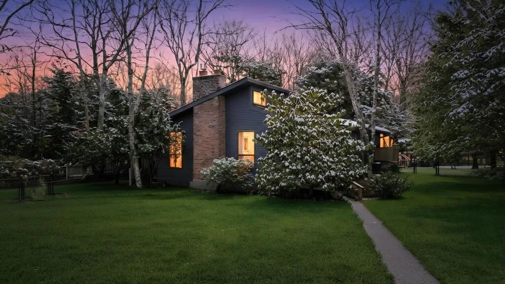 Una casa está entre árboles, junto a un césped y un sendero al anochecer.