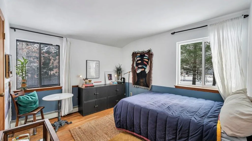 Un dormitorio con una cama, una cómoda y ventanas con vista a árboles.