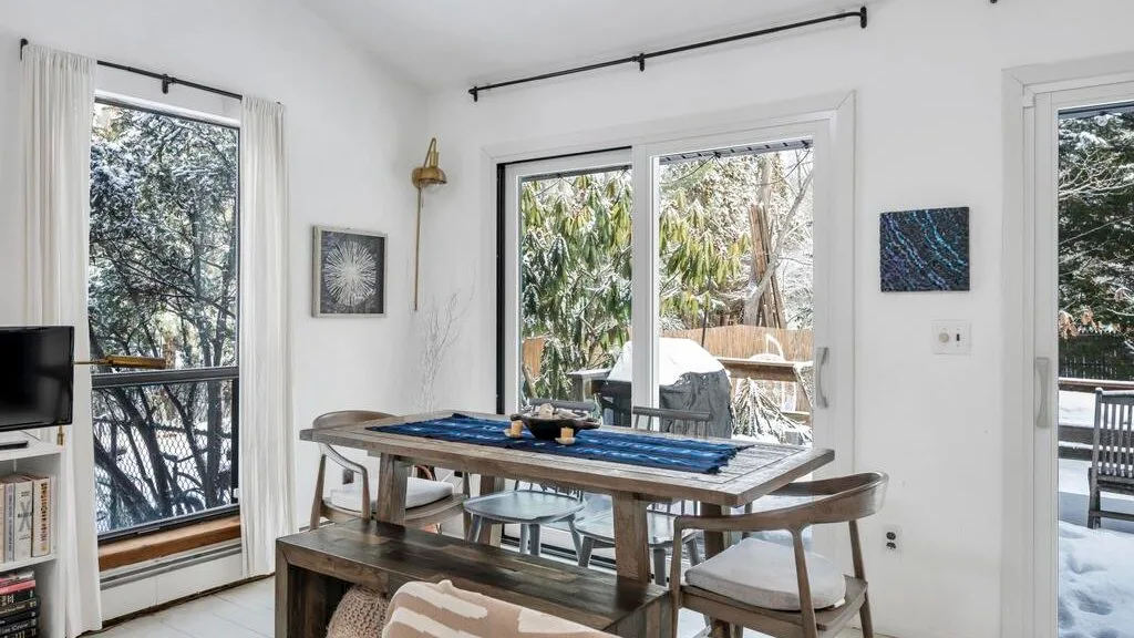 Un comedor luminoso con una mesa de madera y grandes puertas de vidrio que dan a un patio.