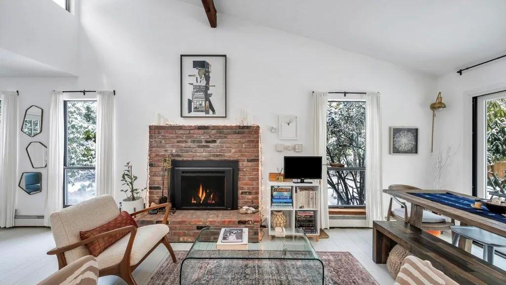 Una sala luminosa cuenta con una chimenea de ladrillo y ventanas grandes.
