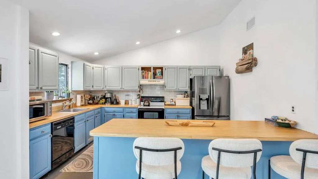 Una cocina luminosa con gabinetes claros, gabinetes inferiores azules y una barra larga.