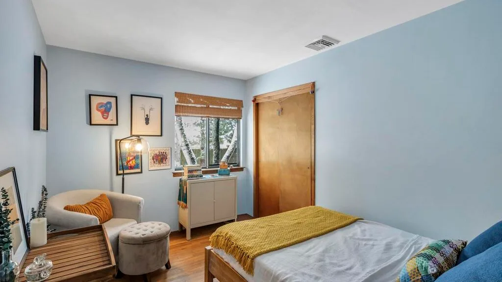 Un dormitorio con una cama, asientos, cuadros enmarcados y una ventana.