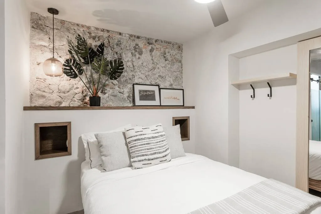 Bedroom with queen bed, textured stone accent wall, and floating wooden shelf