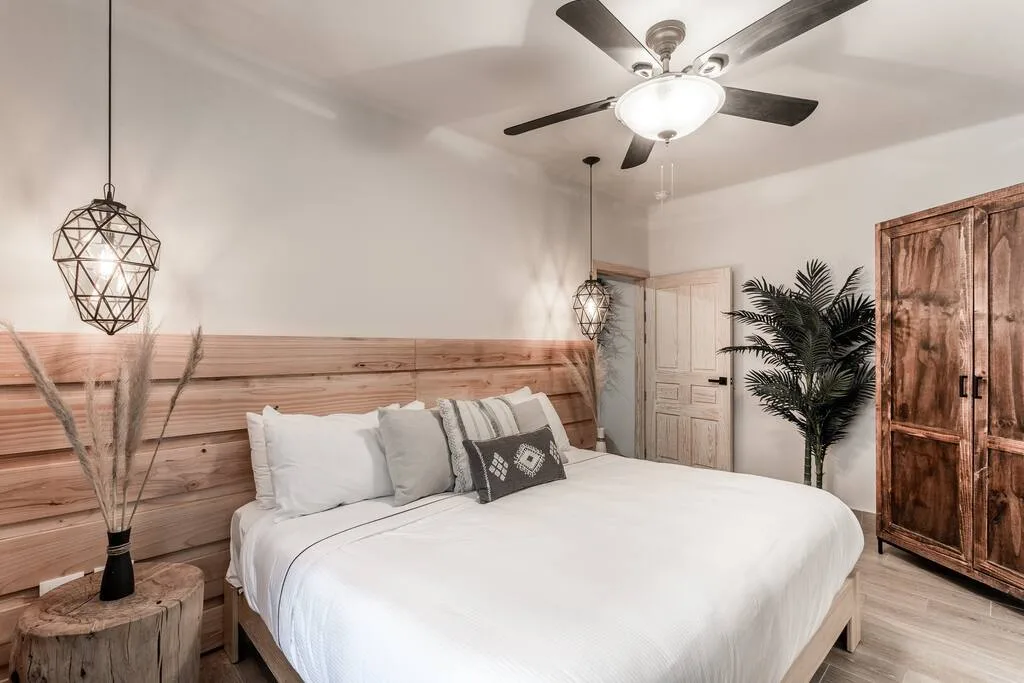 Bedroom with king bed, wooden headboard, and geometric pendant lights overhead