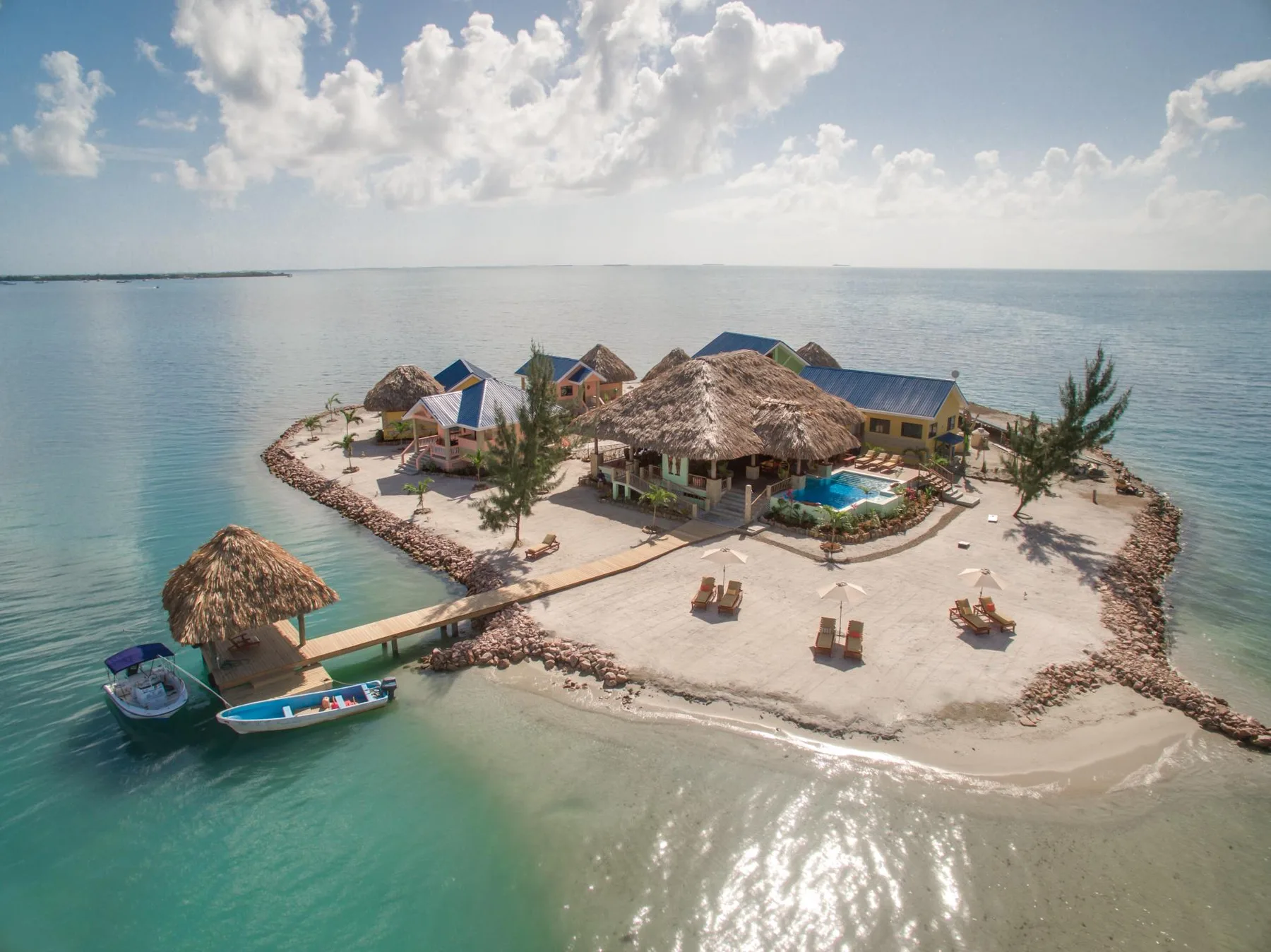 A small island resort sits in calm turquoise water beneath a partly cloudy sky.