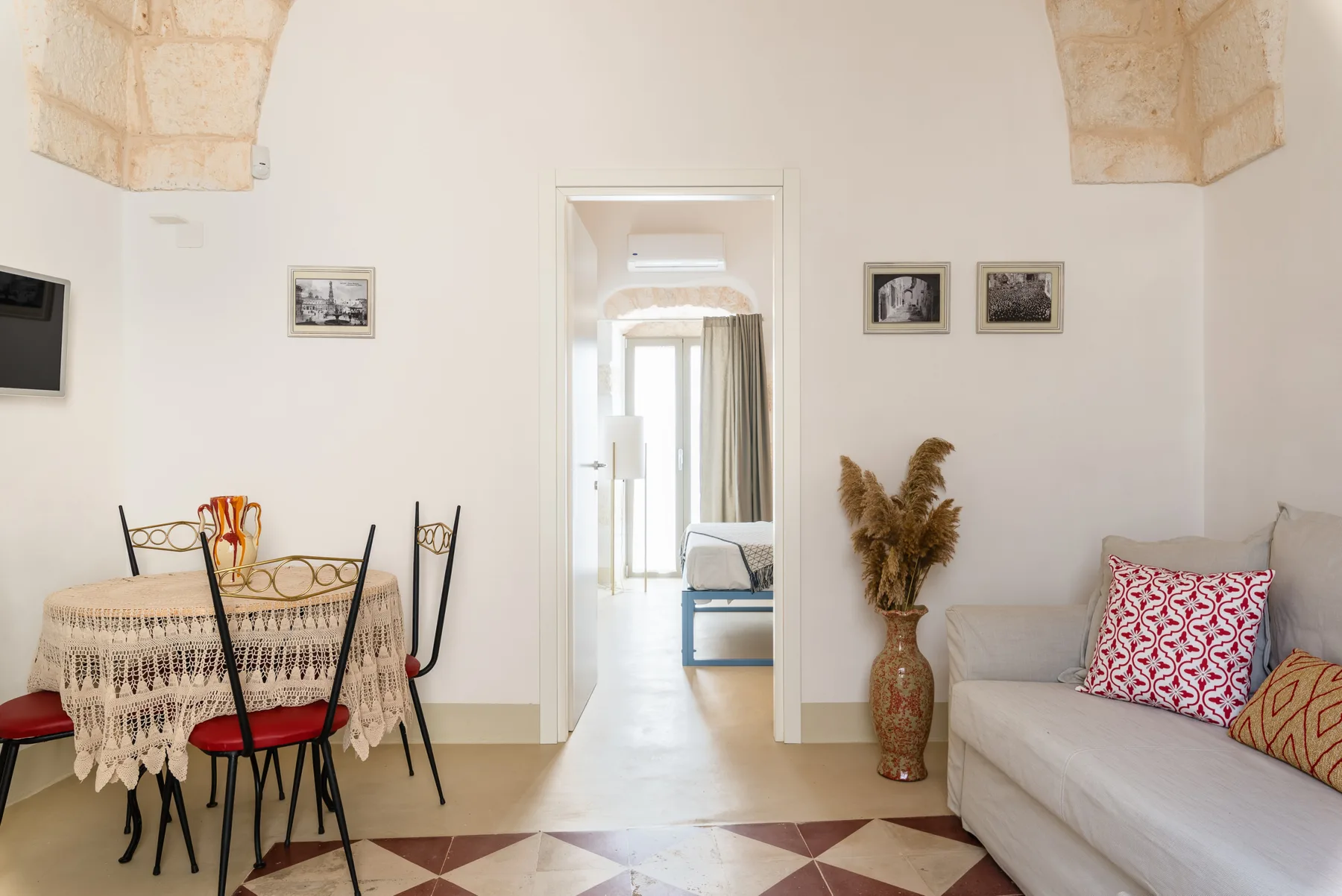 A bright living room with a round dining table, seating, and a doorway to another room.