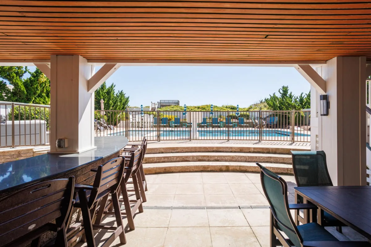 A shaded outdoor dining area overlooks a pool and surrounding greenery.
