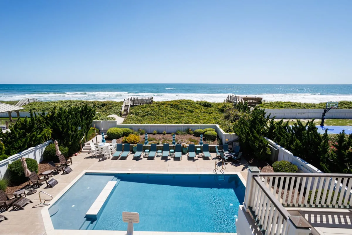 An outdoor swimming pool overlooks a landscaped path and the ocean.