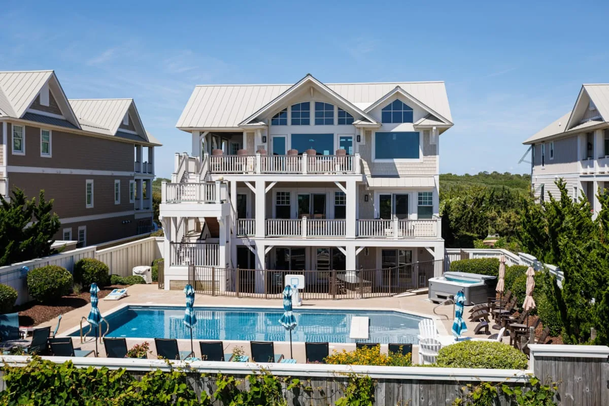 A large multi-story house overlooks an outdoor swimming pool and surrounding deck.