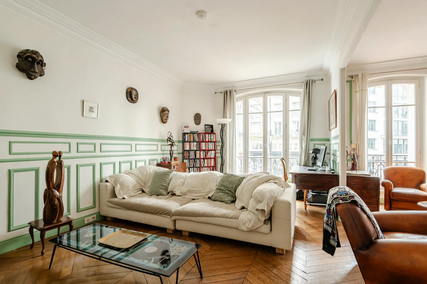 A bright living room with pale seating and tall windows.