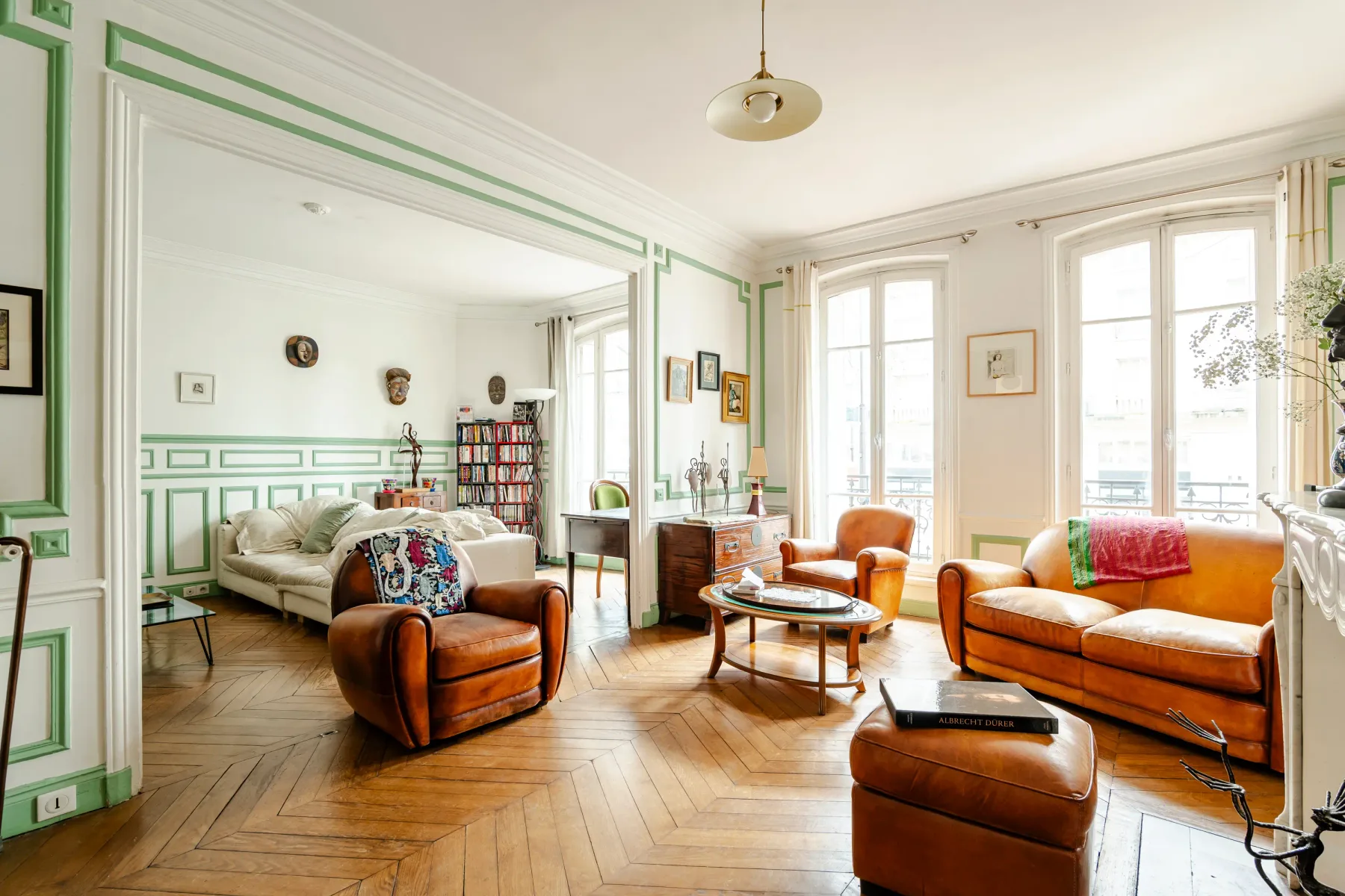 A bright living room with green trim and seating beside tall windows.