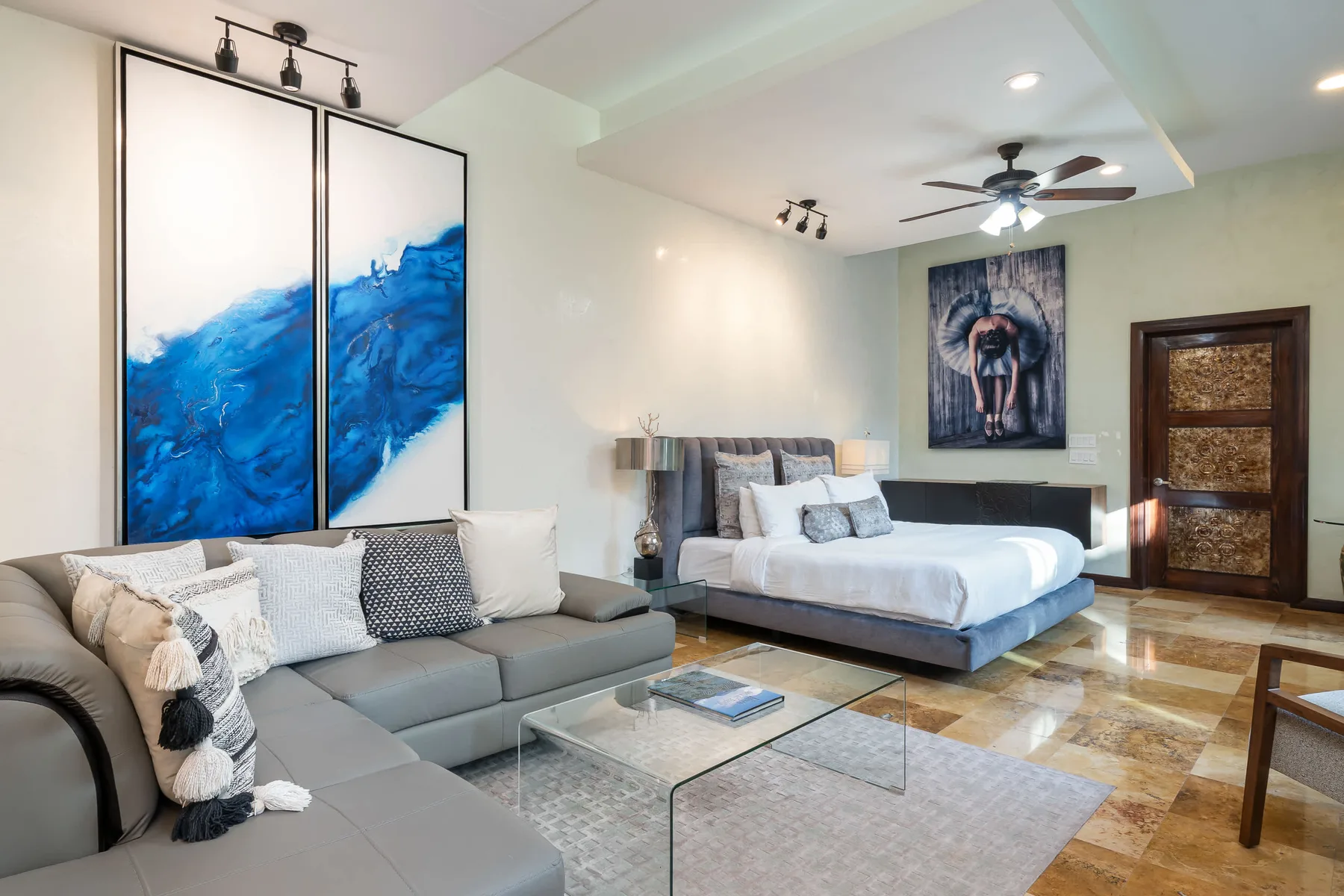 Un dormitorio con una cama, una zona de asientos y una gran obra de arte azul.