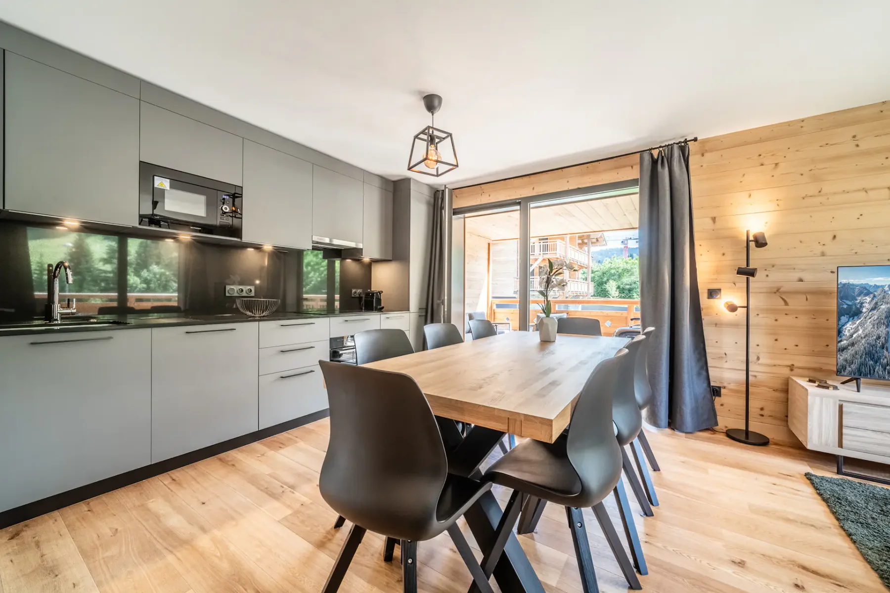 Una cocina moderna con comedor, mesa larga de madera y asientos oscuros.