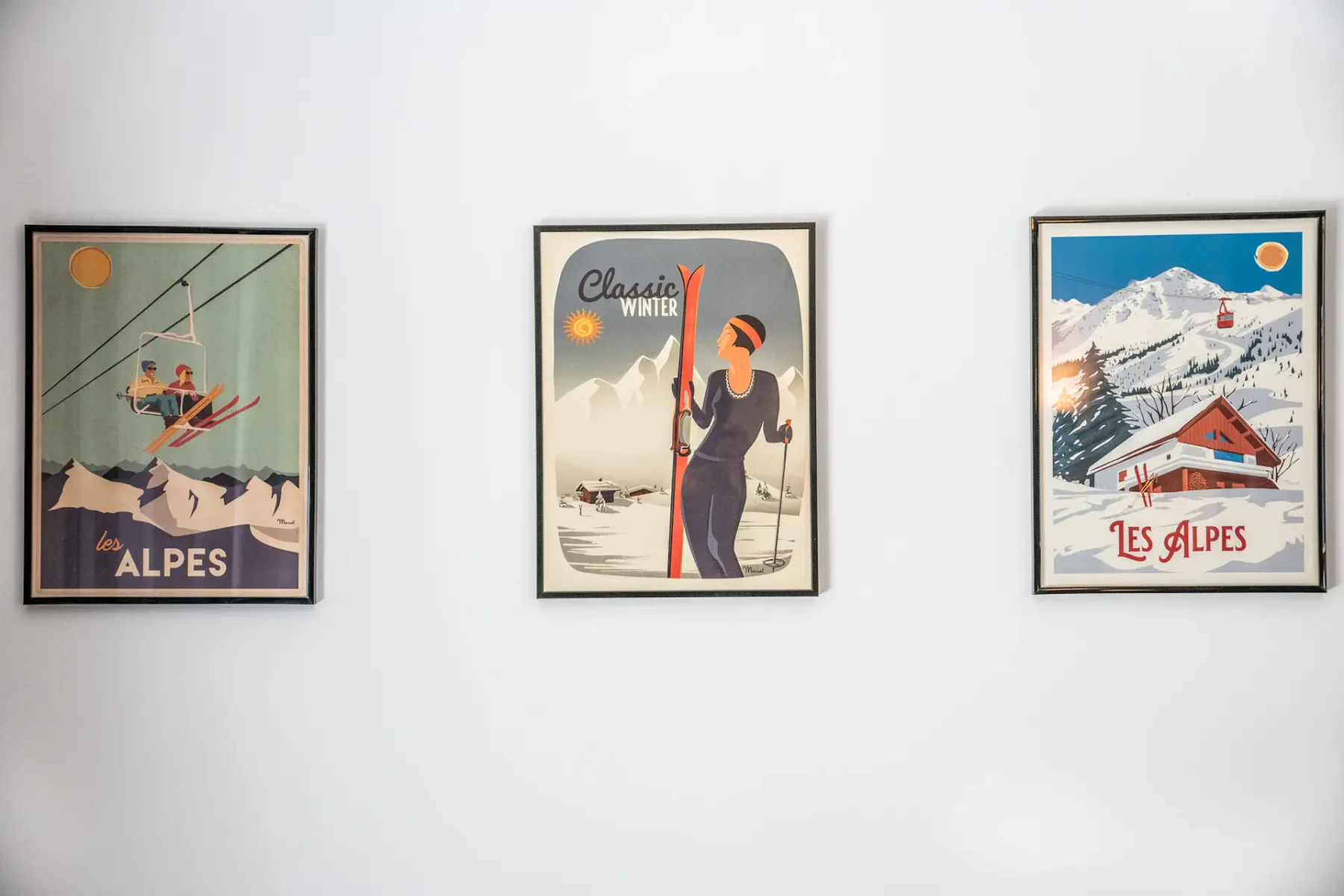 Una pared blanca muestra tres carteles alpinos de estilo vintage enmarcados.