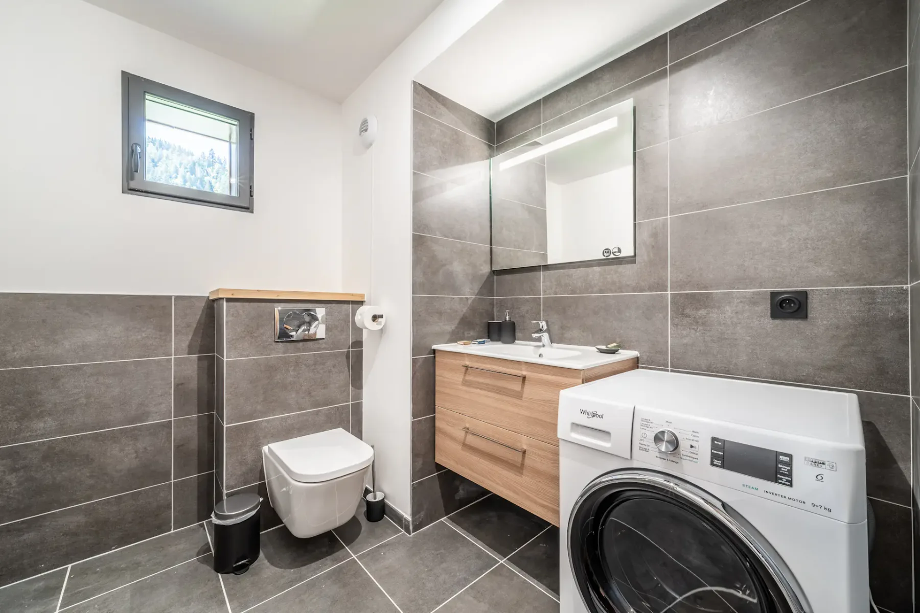 Baño alicatado con inodoro, lavabo y lavadora de carga frontal.