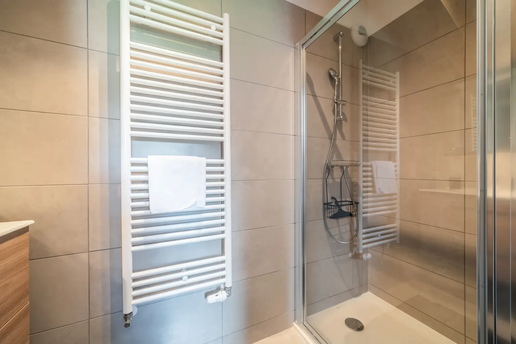 Baño alicatado con ducha de vidrio y toallero térmico blanco.
