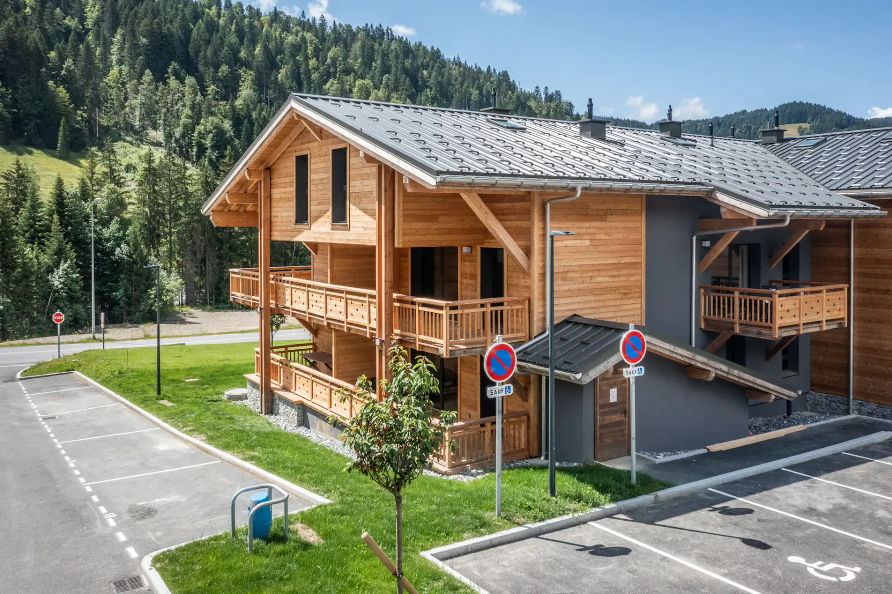 Un edificio de madera en la montaña está junto a un aparcamiento, con laderas boscosas al fondo.