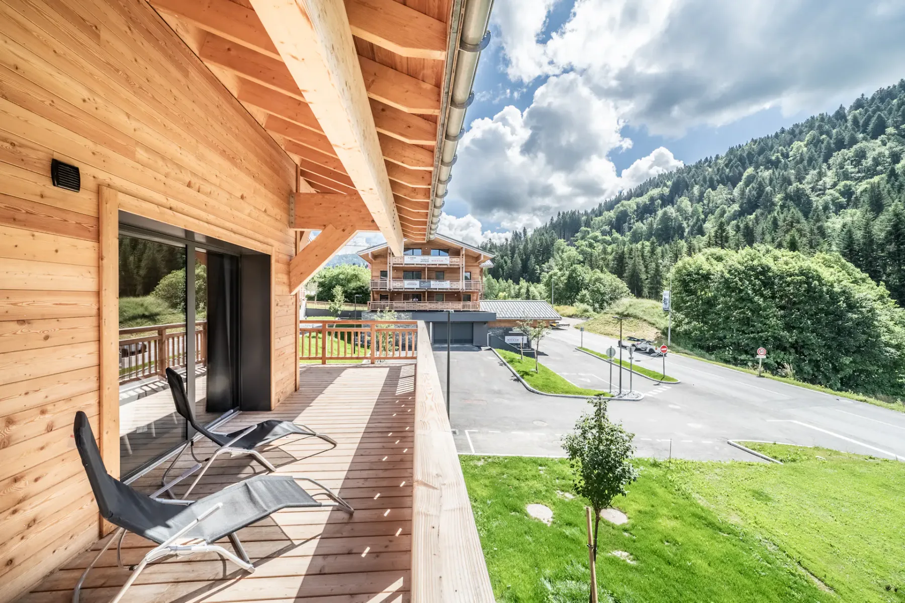 Una terraza de madera con asientos al aire libre da a una ladera verde y edificios cercanos.