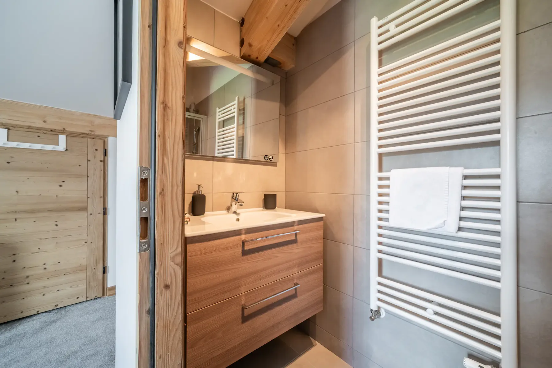 Un baño con mueble de madera, espejo y toallero calefactable en la pared.