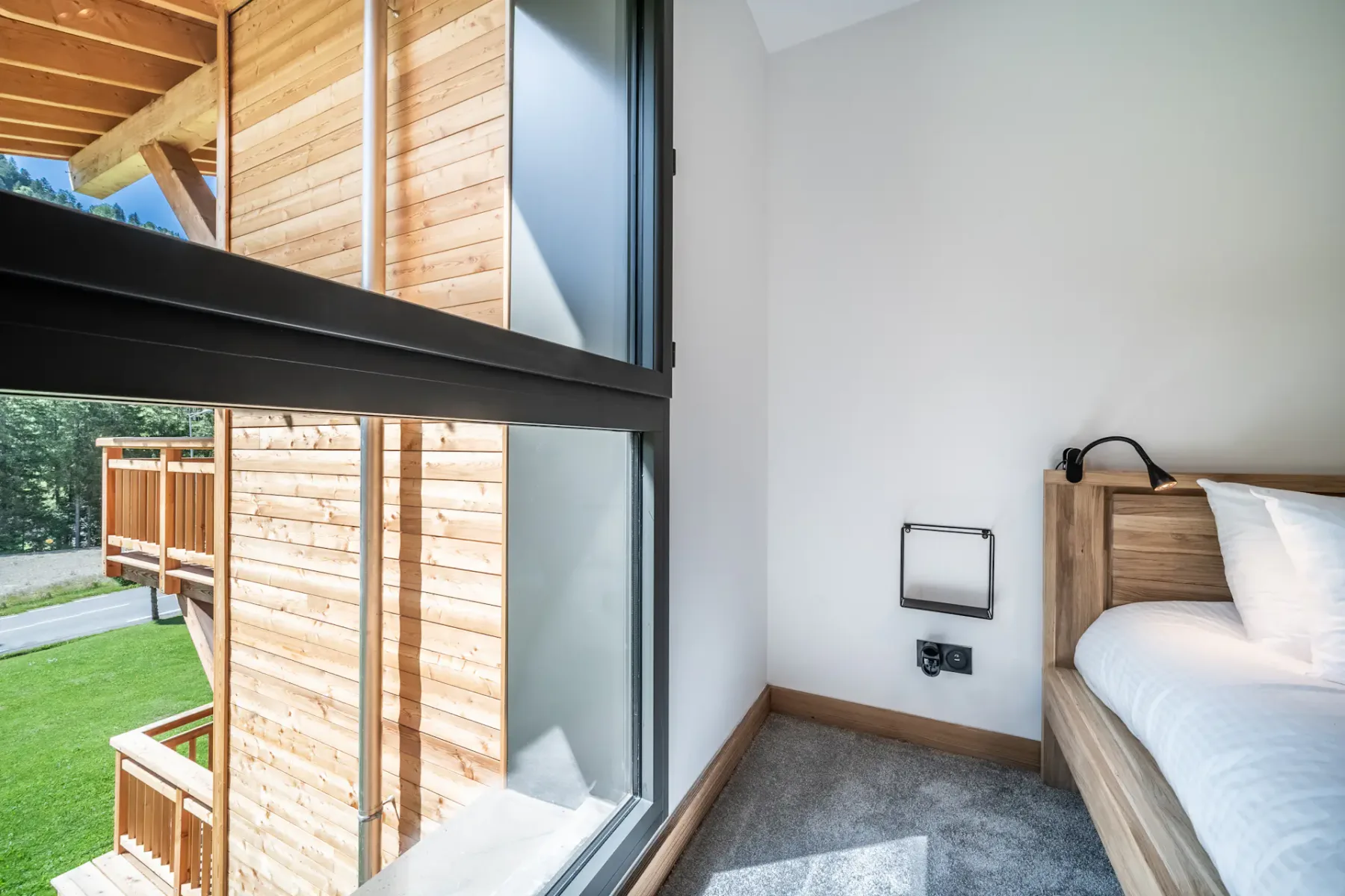 Dormitorio con una cama junto a grandes ventanas con vistas a un exterior de madera.
