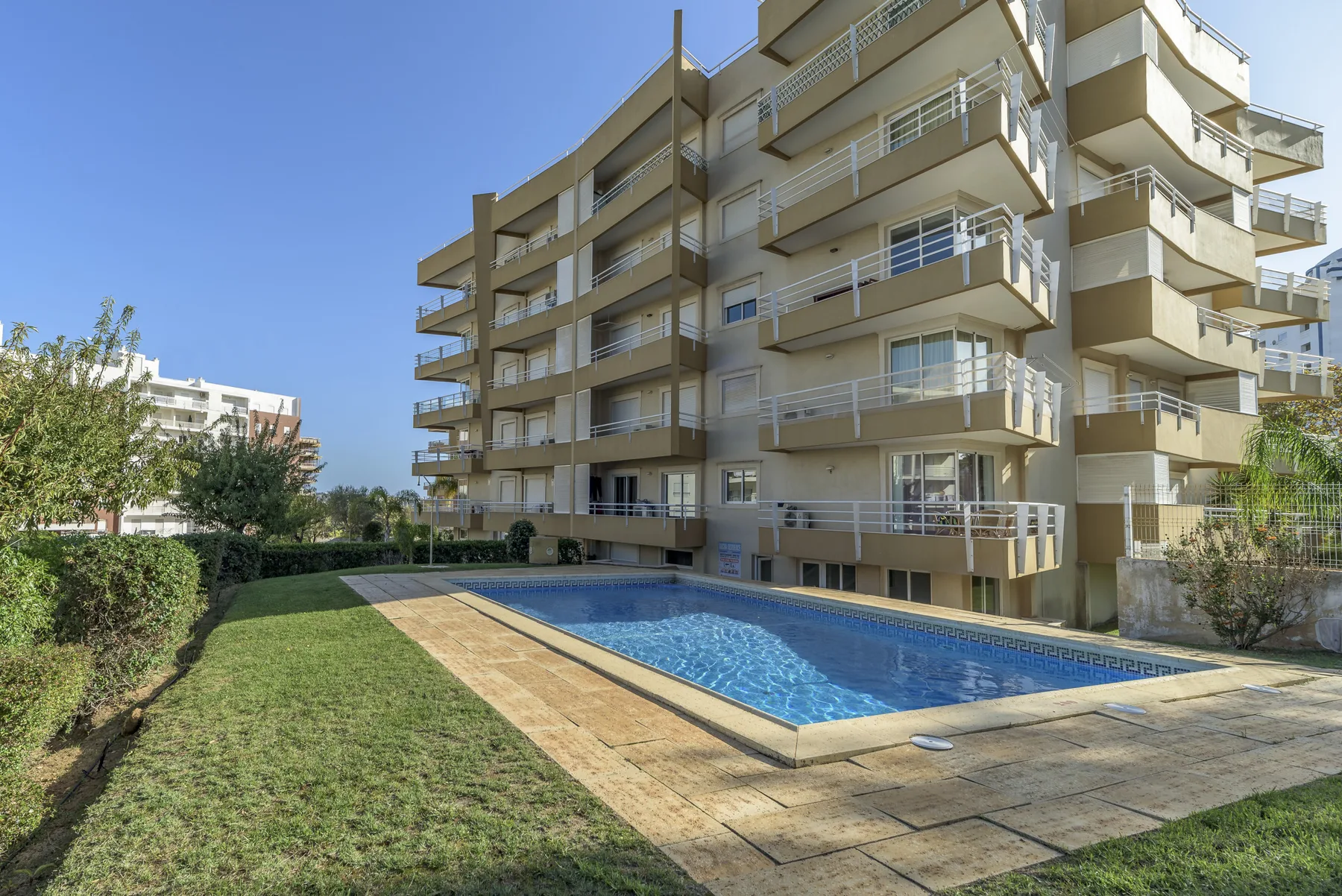 A modern apartment building overlooks an outdoor swimming pool and landscaped lawn.