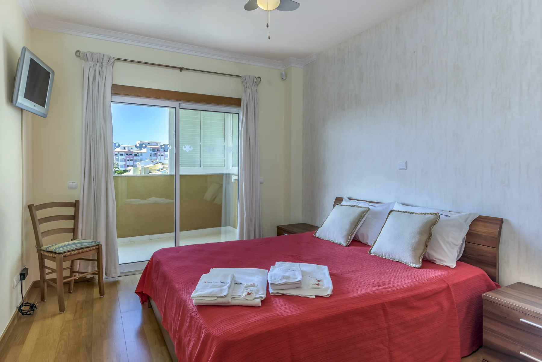 Un dormitorio con una cama cubierta de rojo, cabecero de madera y puertas correderas de cristal.