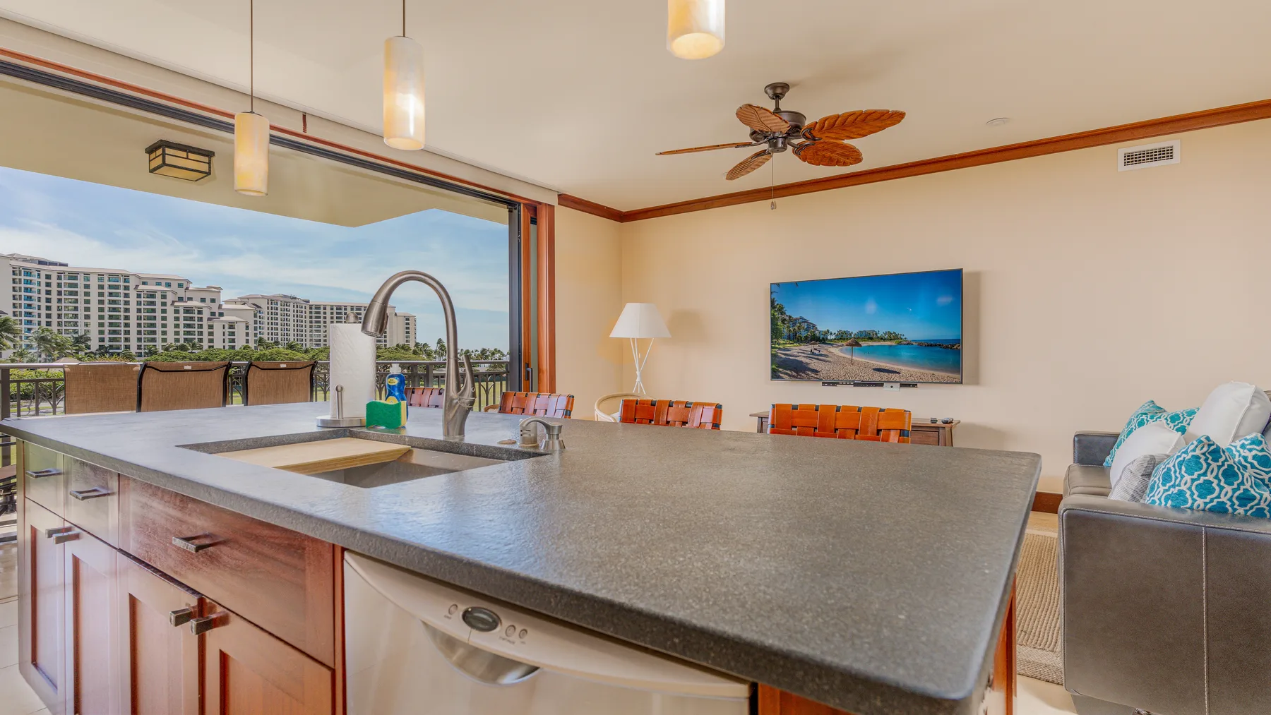 An open kitchen with a large island overlooks a furnished balcony and nearby buildings.