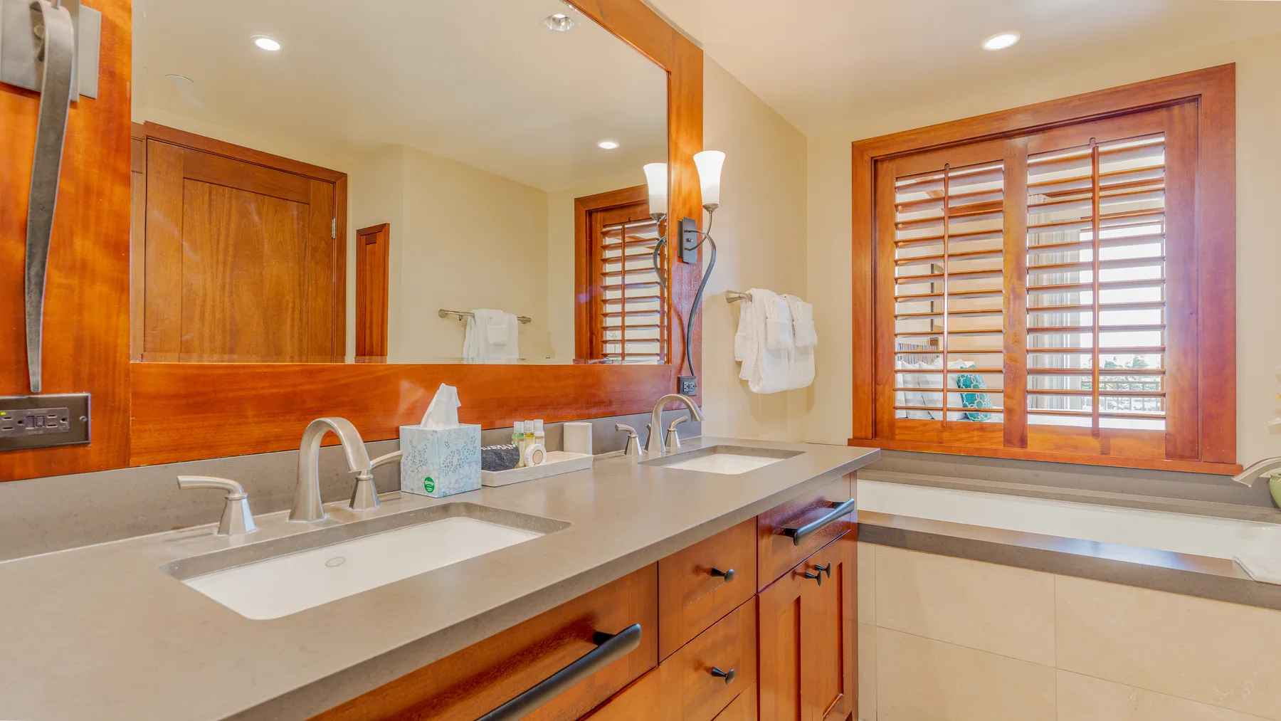 A bathroom vanity with a wide mirror and a window with wooden blinds.