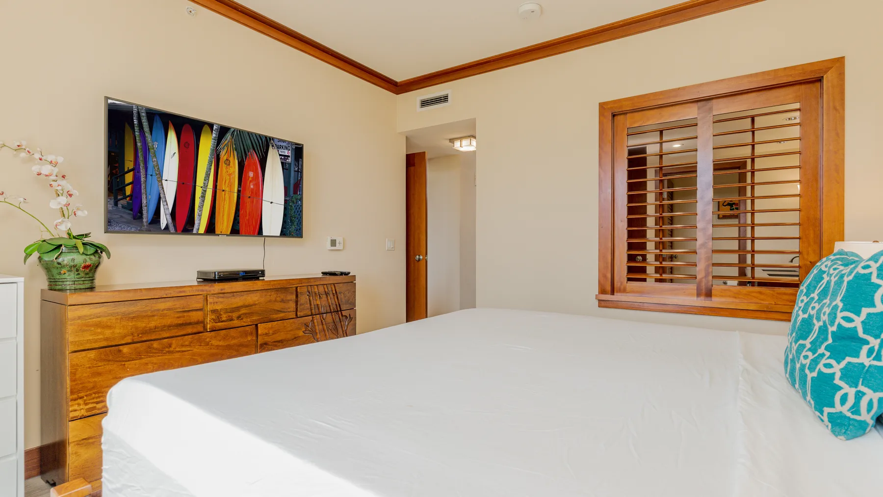 A bedroom with a neatly made bed, a wooden dresser, and colorful wall art.
