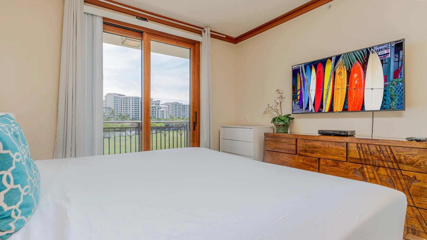 A bedroom with a large bed, sliding glass doors, and a dresser beneath colorful wall art.