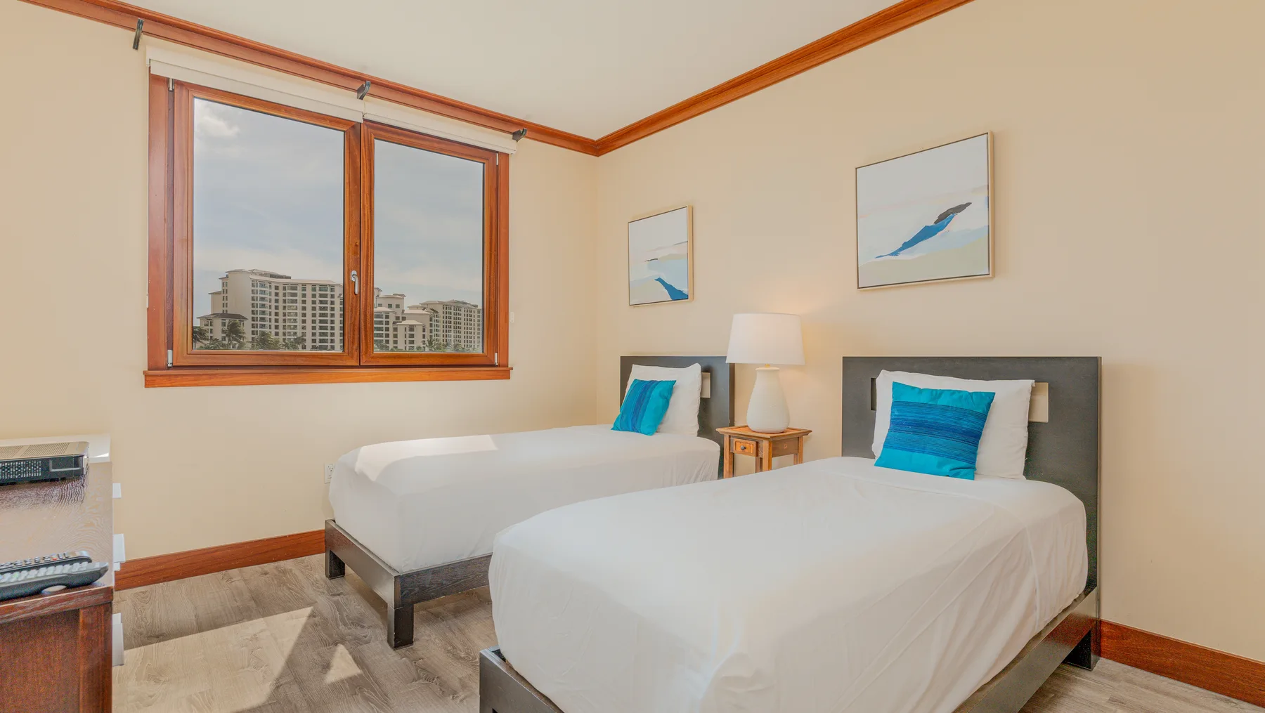 A bedroom with two beds, a bedside table, and large windows.