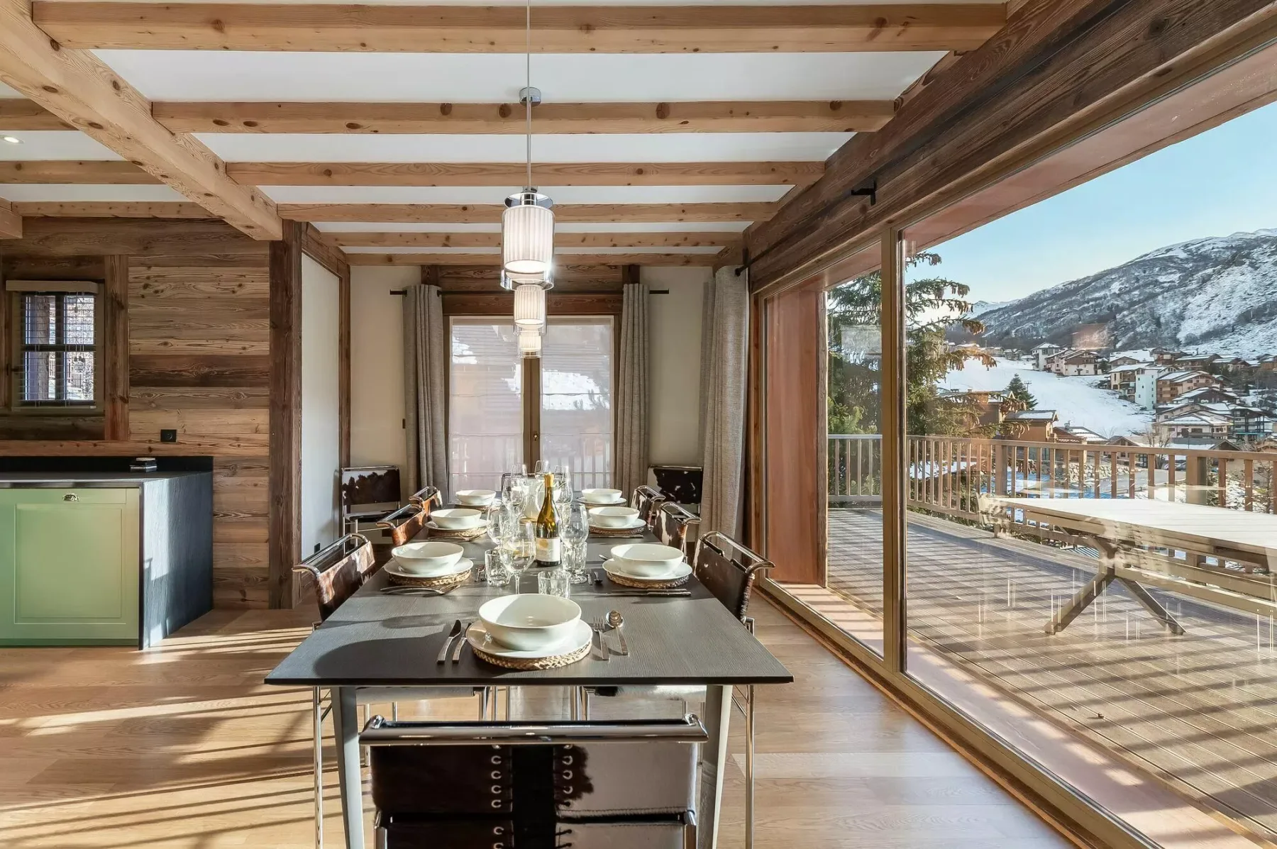 A dining area with a long table beside large windows overlooking a snowy hillside.