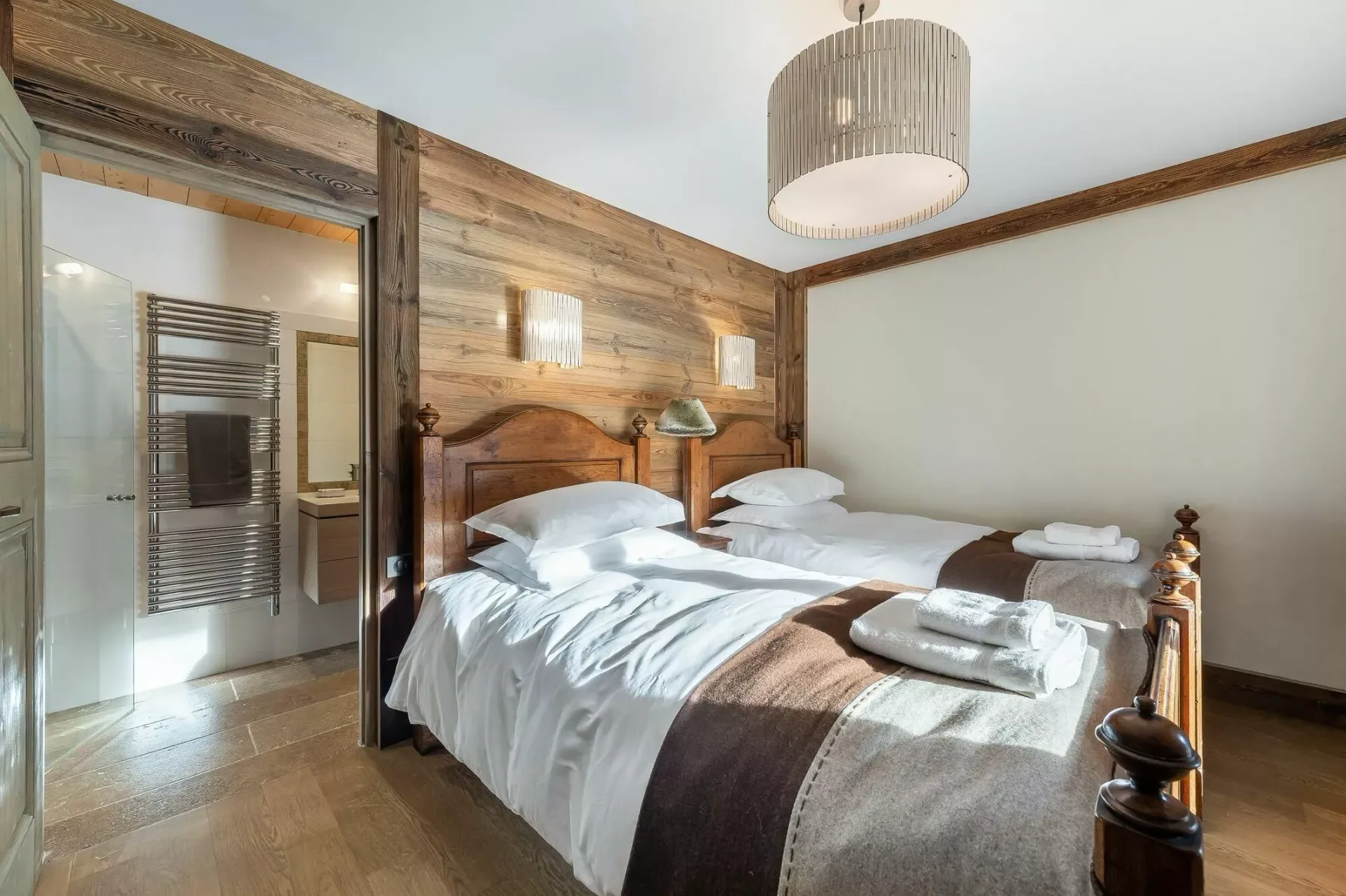 A bedroom with two beds, white linens, and a glass-walled bathroom beside it.