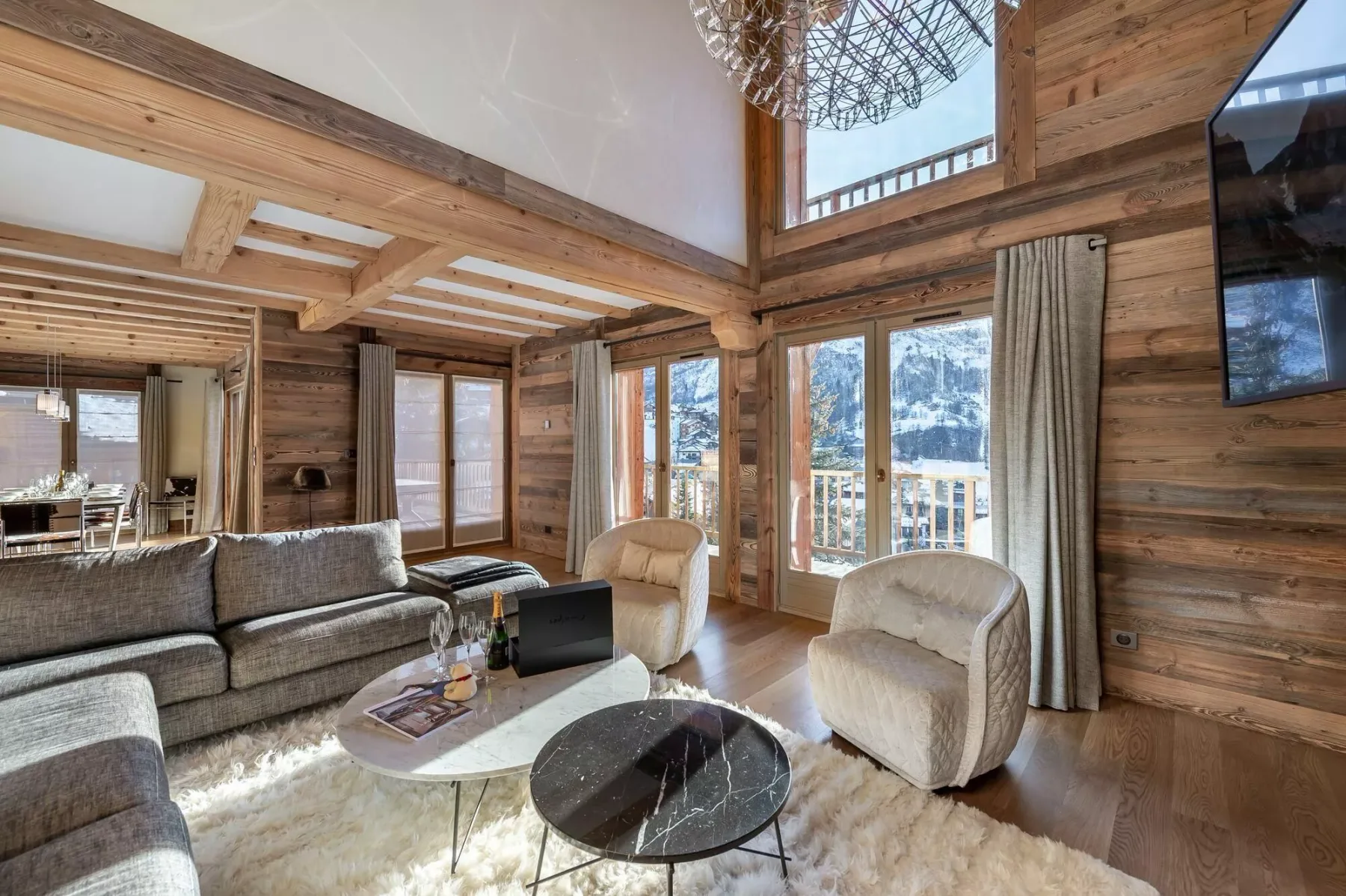 Una sala de estar revestida de madera, con asientos y grandes ventanas con vistas a un paisaje nevado.