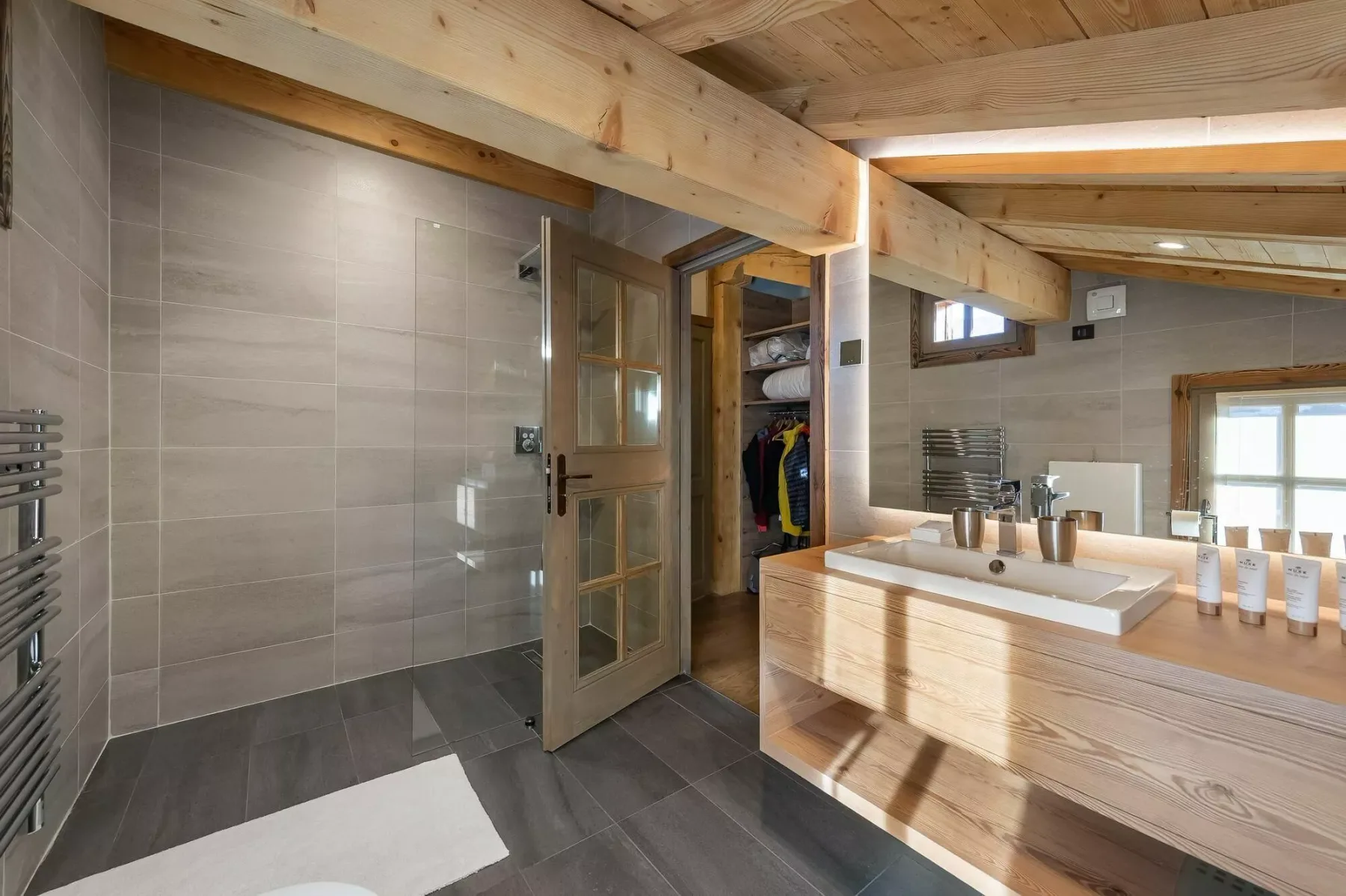 A tiled bathroom with a glass-paneled door and a wooden vanity.