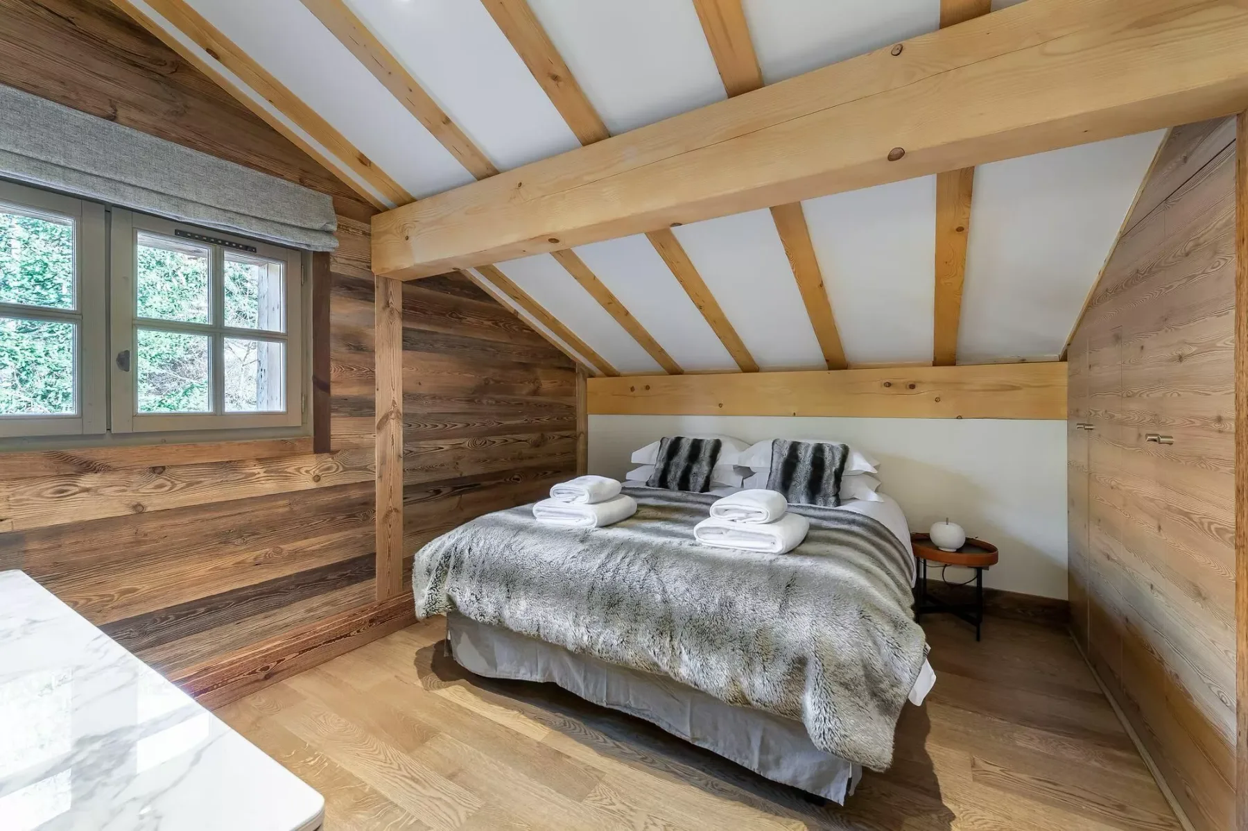 A bedroom with a double bed, striped pillows, and exposed wooden beams.