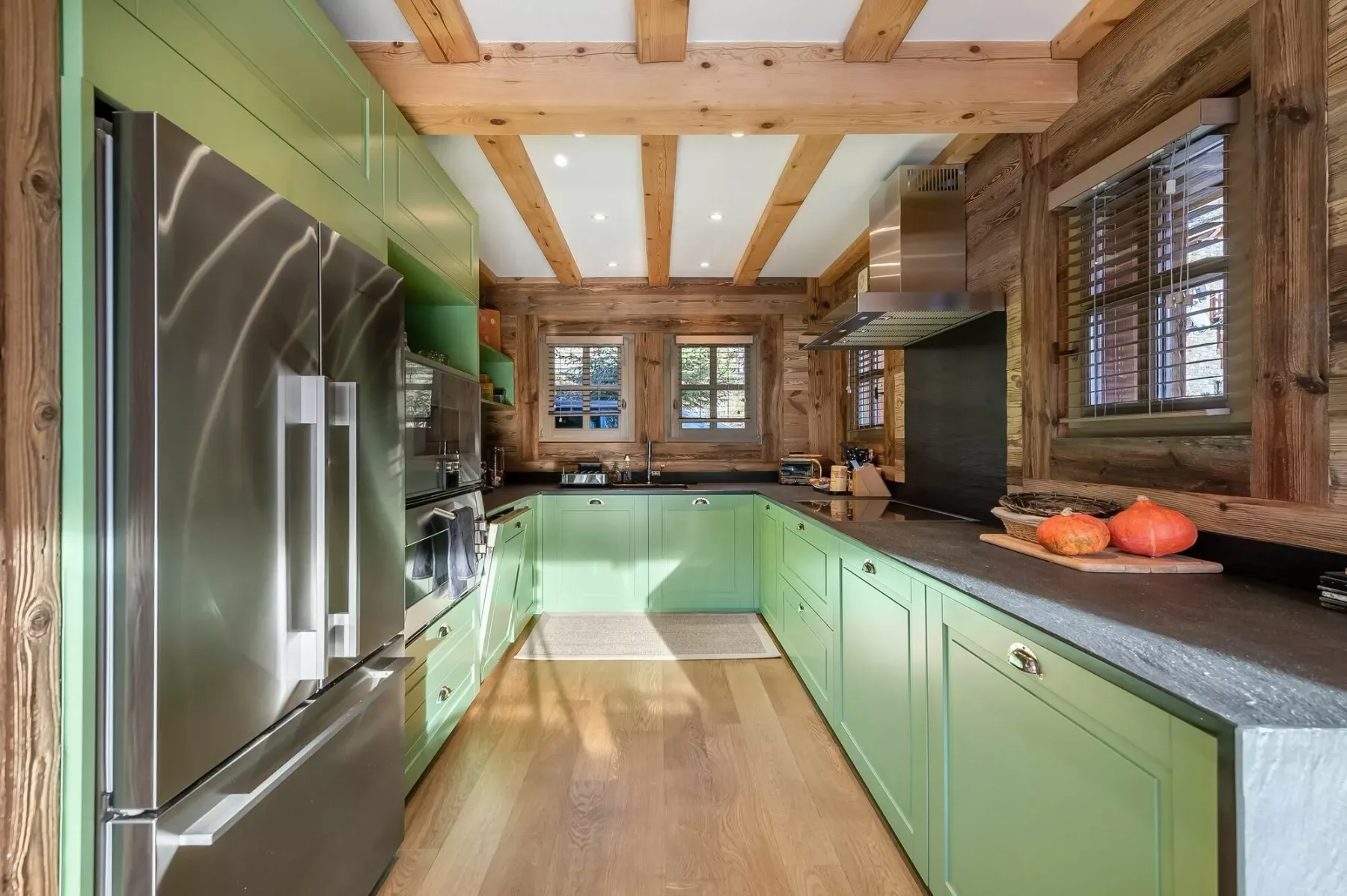 A kitchen with green cabinets, stainless steel appliances, and wooden ceiling beams.