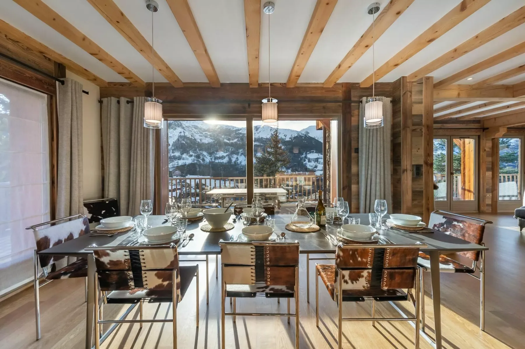 A dining area with a long table set for a meal beside large windows.