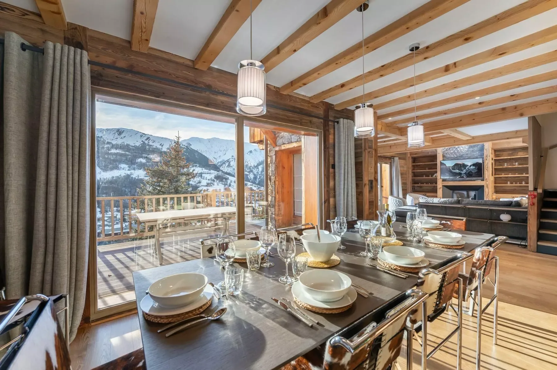 A dining area with a set table beside large windows overlooking a snowy mountain view.